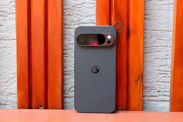 Google Pixel smartphone with camera and G logo against a wooden wall, illustrating the theme of expanding AI features beyond Pixel devices