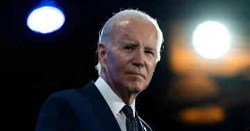 Joe Biden in ernster Stimmung vor hellen Scheinwerfern, die seinen kritischen Gesundheitszustand widerspiegeln