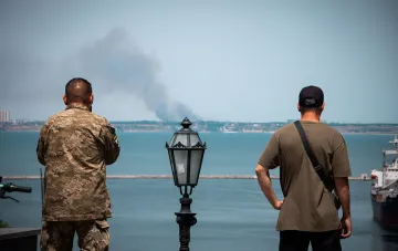 Soldier and civilian observe smoke rising over Odesa after Russian attack on energy infrastructure on August 9, 2026