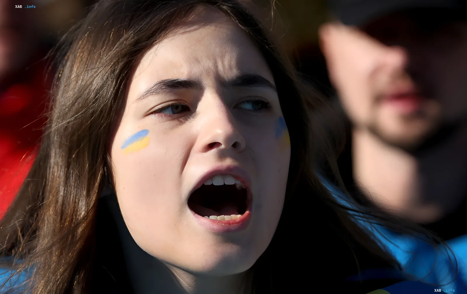 Украинская девушка с флагом на лице кричит в поддержку армии, отражая общественные настроения 2026 года
