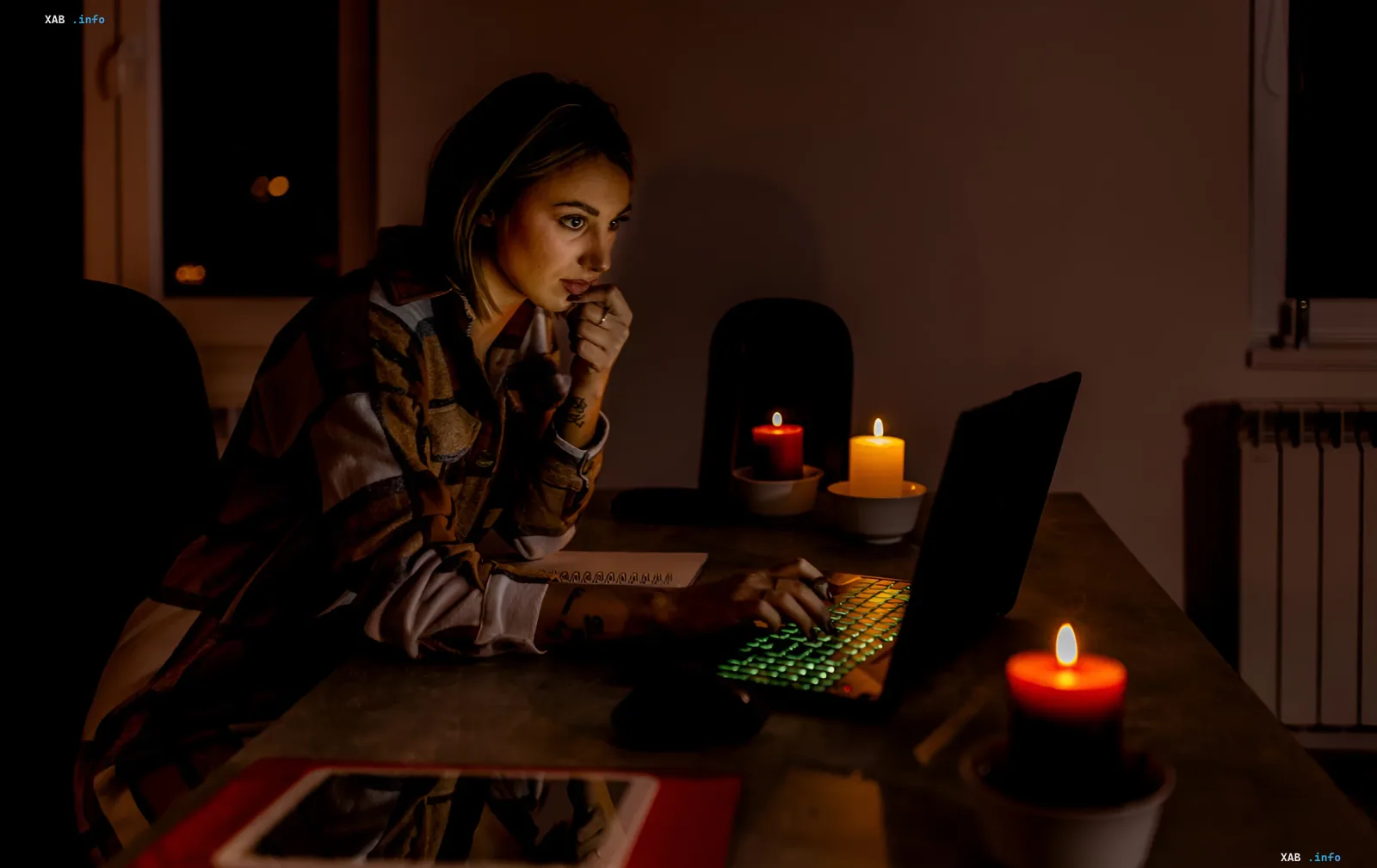 Woman working on laptop by candlelight in dark room — symbol of energy crisis in Odesa after Russian strike