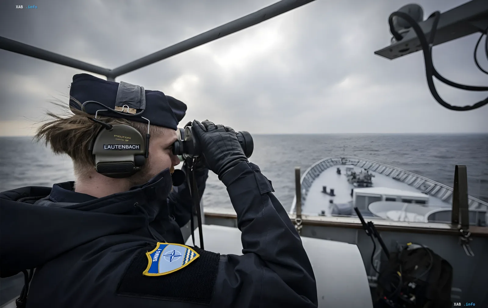 Моряк ВМС Германии с опознавательным знаком НАТО наблюдает за горизонтом в бинокль с палубы корабля