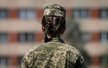 Спина жінки у військовій формі з косами, що символізує тему мобілізації жінок, спростовану РНБО