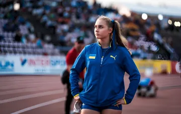 Поліна Дзерожинська в синій спортивній формі з українським прапором та логотипом Puma на ЮЧМ в Юджині, де встановила три рекорди та увійшла до топ-5 світу