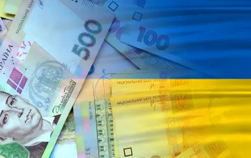 Украинские гривневые купюры на фоне флага Украины — символ государственной поддержки бизнеса в условиях военных рисков