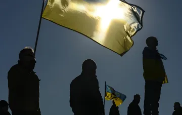 Силуэты людей с украинскими флагами на фоне заката, символизирующие стойкость и надежду украинцев в условиях войны