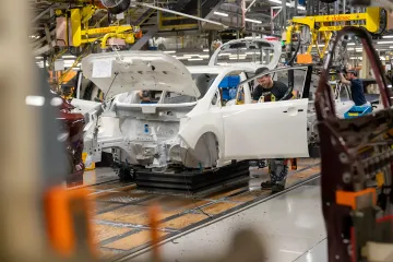 Automotive assembly plant: workers installing parts on a white electric car body, symbolizing the UK auto industry's shift to electric vehicles through government grants