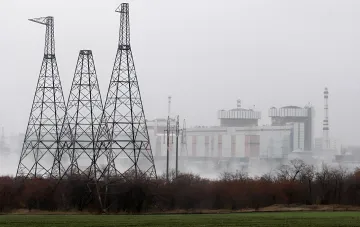 Atomkraftwerk im Nebel mit hohen Metallmasten für Hochspannungsleitungen im Vordergrund, das die Dominanz der Atomenergie in der Struktur des ukrainischen Strommarkts im Jahr 2025 symbolisiert