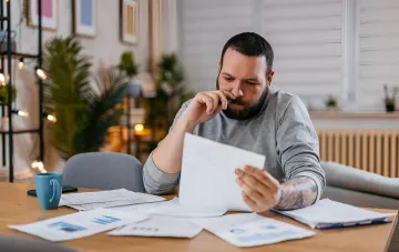 Mann prüft Versorgungsrechnungen und Schulden, sitzt an einem Tisch mit Dokumenten und einer Tasse Kaffee