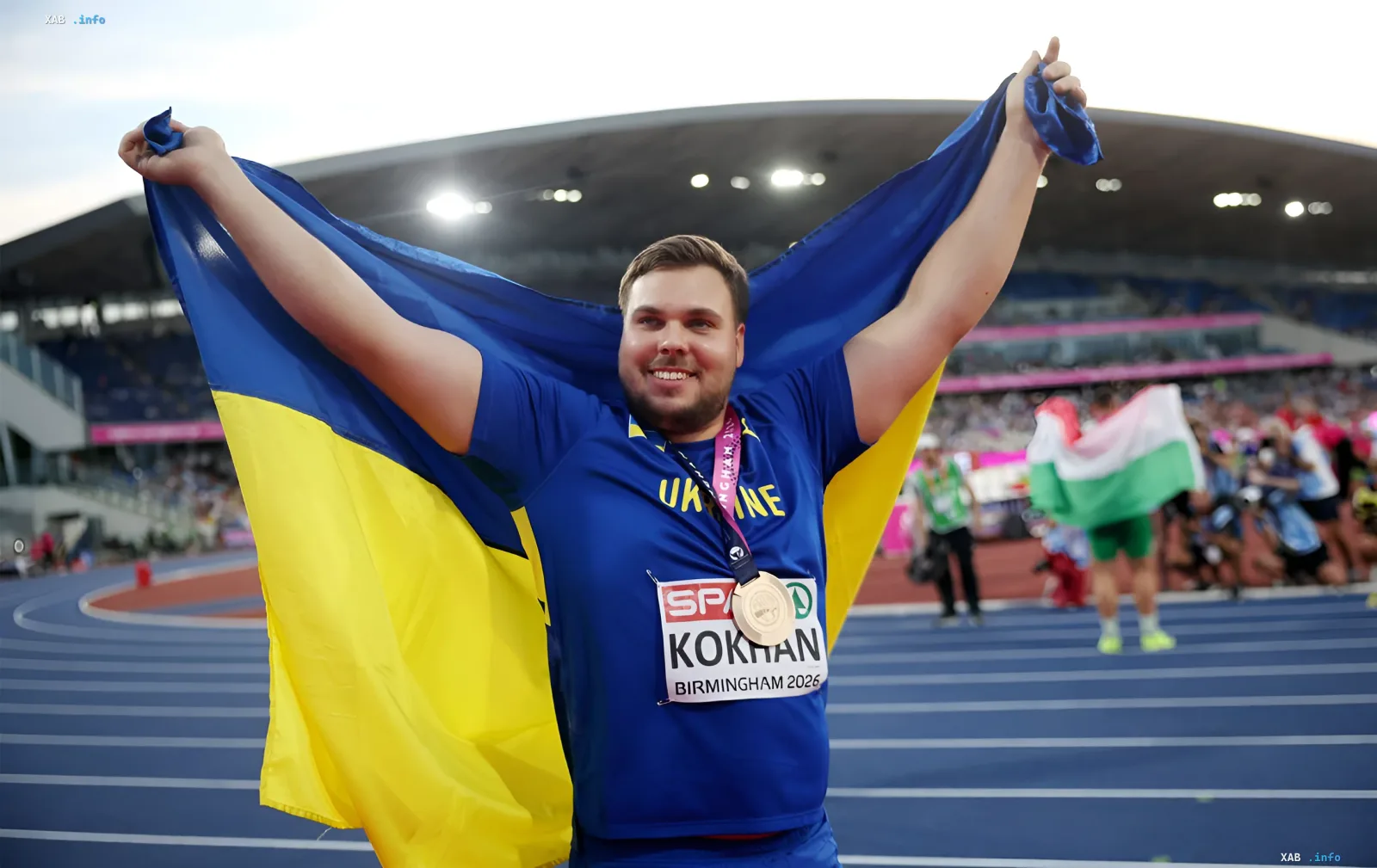 Михаил Кохан с бронзовой медалью ЧЕ-2026 в Бирмингеме, держащий флаг Украины на стадионе
