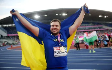 Mykhailo Kokhan with bronze medal from EC-2026 in Birmingham, holding Ukrainian flag on stadium