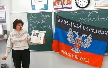 Вчителька в класі з прапором так званої «ДНР» та підручником, що ілюструє введення історії «ДНР» та «Новоросії» в школах РФ з 2026 року
