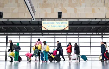 Gruppe ukrainischer Flüchtlinge mit Koffern und Taschen steht am Ausgang eines Bahnhofs in Deutschland unter einem Schild 'Willkommen in Hannover'