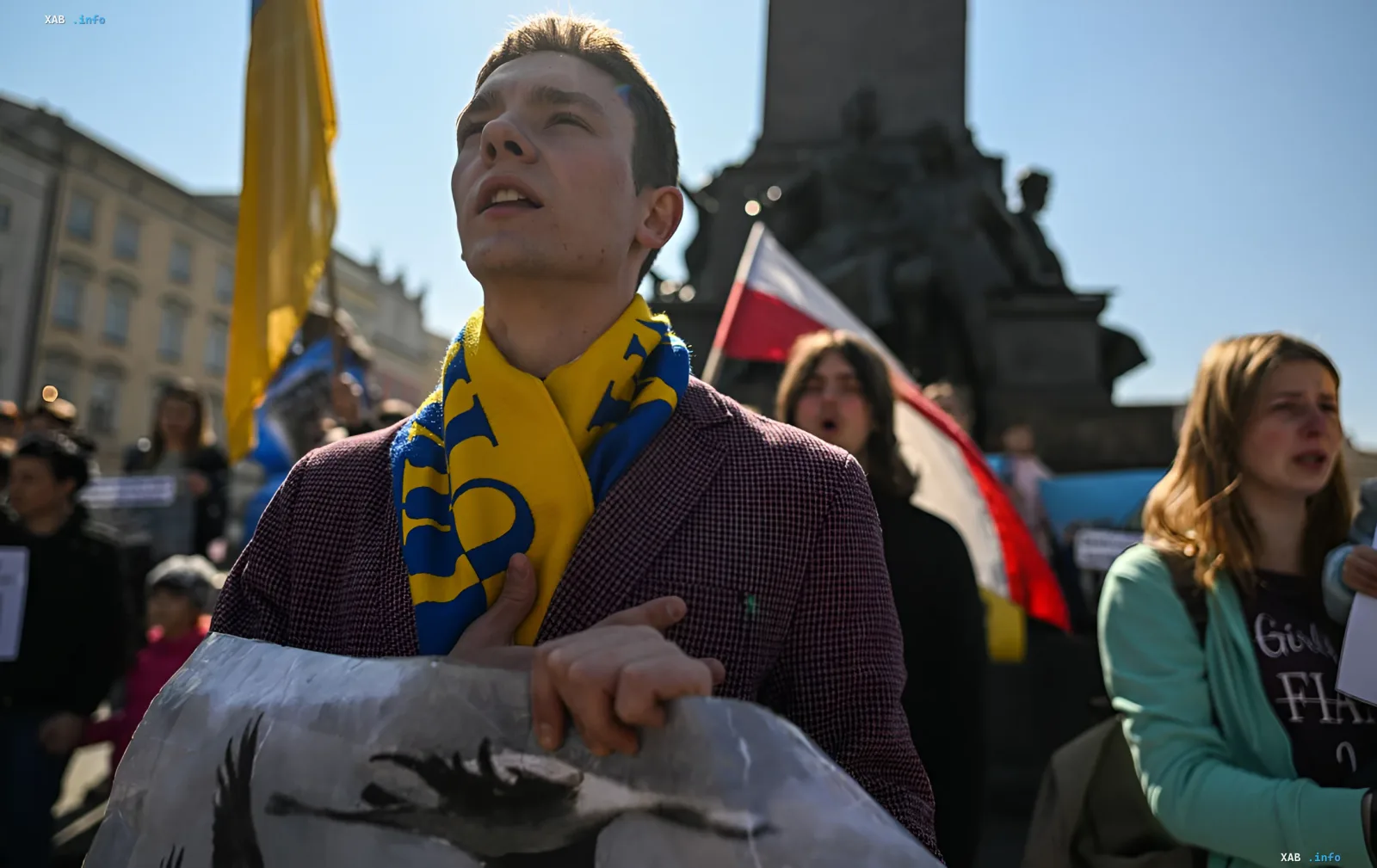 Ukrainischer Aktivist mit ukrainischer Flagge und Schal bei einer Demonstration in Polen vor polnischem Flaggenhintergrund