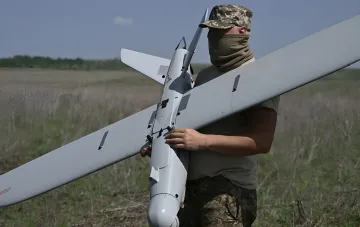 Военнослужащий держит разведывательный дрон на фоне поля, иллюстрируя тему отмены «Дронницы-2026» в Великом Новгороде из-за угрозы украинских ударов