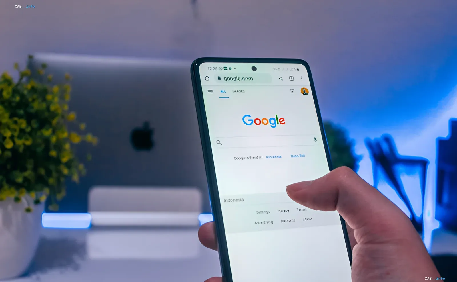 Smartphone displaying Google homepage, with modern workspace in background; visual for news on French media demanding compensation from Google over AI summaries causing 38% traffic drop
