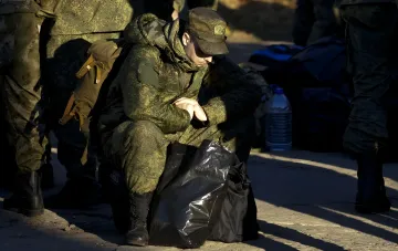 Уставший российский солдат в камуфляже сидит на земле с рюкзаком, символизируя потери и усталость армии