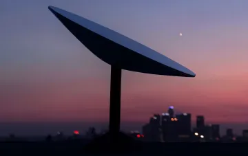 Антенна Starlink на закате с силуэтом города на фоне — символ спутникового интернета, который Польша обвиняет в дискриминации