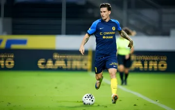 Украинский легионер в синей форме с логотипом Cinkarna Grawe dribблирует мяч на поле во время матча квалификации Лиги чемпионов 2026/27