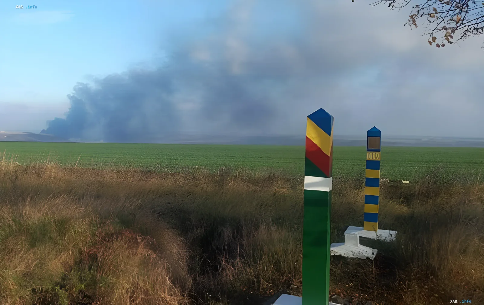 Smoke from drone explosion over field in Moldova near Ukrainian border, with border posts featuring flags nearby