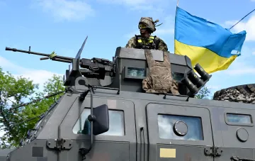 Ukrainischer Soldat auf gepanzertem Fahrzeug mit ukrainischer Flagge und Maschinengewehr, Symbol für taktische Änderungen der AFU im Jahr 2026
