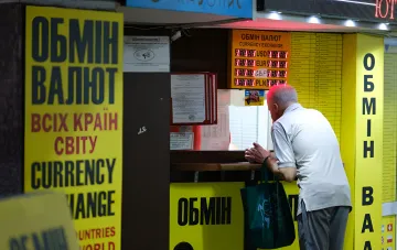 Мужчина у окна обменного пункта с вывеской «Обмін валют» — иллюстрация к новости о ужесточении контроля НБУ за валютными операциями, включая дробление сделок