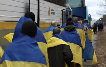 Украинские военнопленные, завернутые в национальные флаги, готовятся к посадке в автобус для обмена
