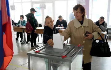 Женщина и мальчик опускают бюллетень в урну на оккупированной территории Украины, иллюстрируя предупреждение ЦИК об опасности участия в российских выборах.