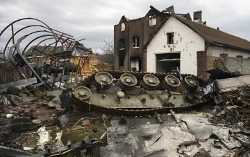 Zerstörte russische Panzerkette und Trümmer von Militärfahrzeugen vor einem beschädigten Haus