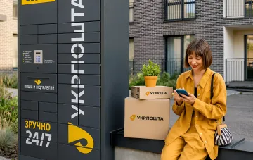 Женщина проверяет заказ на смартфоне рядом с почтоматом Укрпочта в жилом комплексе, символизируя удобство получения посылок 24/7