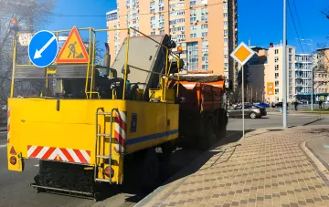 Gelbes Kommunalfahrzeug mit Verkehrsschildern auf der Südbrücke in Kiew, bereit für großangelegte Reparaturarbeiten an der Hochstraße im August 2026