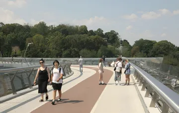 Люди гуляют по пешеходному мосту в солнечный день, иллюстрируя жаркую погоду в Закарпатье из-за антициклона