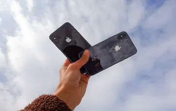Рука держит два черных iPhone X на фоне неба, символизируя конец эпохи устройства после признания Apple его устаревшим