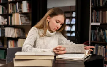 Молодая женщина в библиотеке изучает старинную книгу, исследуя историю своих предков