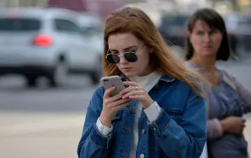 Junge Frau mit Brille schaut auf ihr Smartphone auf der Straße, symbolisiert den Übergang von 3G zu modernen Kommunikationsnetzen