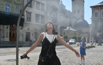 Frau genießt kühle Gischt aus einem Straßenbrunnen in einer ukrainischen Stadt, ein Symbol der Erleichterung bei der +33°C-Hitzewelle im August 2026