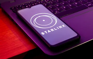 Логотип Starlink на экране смартфона, лежащего на ноутбуке, символизирующий возвращение Польши в зону покрытия спутникового интернета
