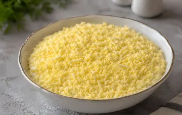 White bowl with grated cheese, ingredient for the nostalgic salad 'Pufik' with chicken and apple
