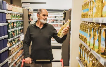 Älterer Mann mit Bart wählt Pflanzenöl im Supermarkt, symbolisiert die Widerstandsfähigkeit des ukrainischen Lebensmittelsystems