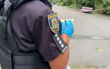Полицейский в защитном жилете и синих перчатках фиксирует улики на месте стрельбы в парке Лубен, где мужчина открыл огонь по сотрудникам МВД