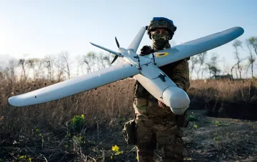 Український солдат тримає бойовий дрон на фоні поля, ілюструючи залежність України від імпорту дронів та вплив митних зборів Трампа на оборону