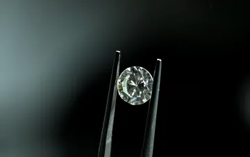 Perfekter runder Diamant, von Pinzette gehalten auf dunklem Hintergrund — Symbol für die Zugänglichkeit von Labordiamanten