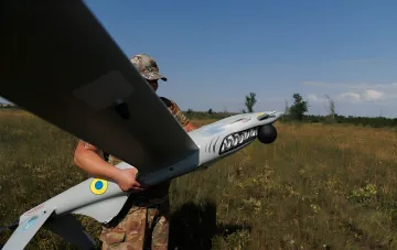 Украинский военный готовит к запуску разведывательный дрон с символикой ВСУ на фоне поля, иллюстрируя тему борьбы с ретрансляторами противника
