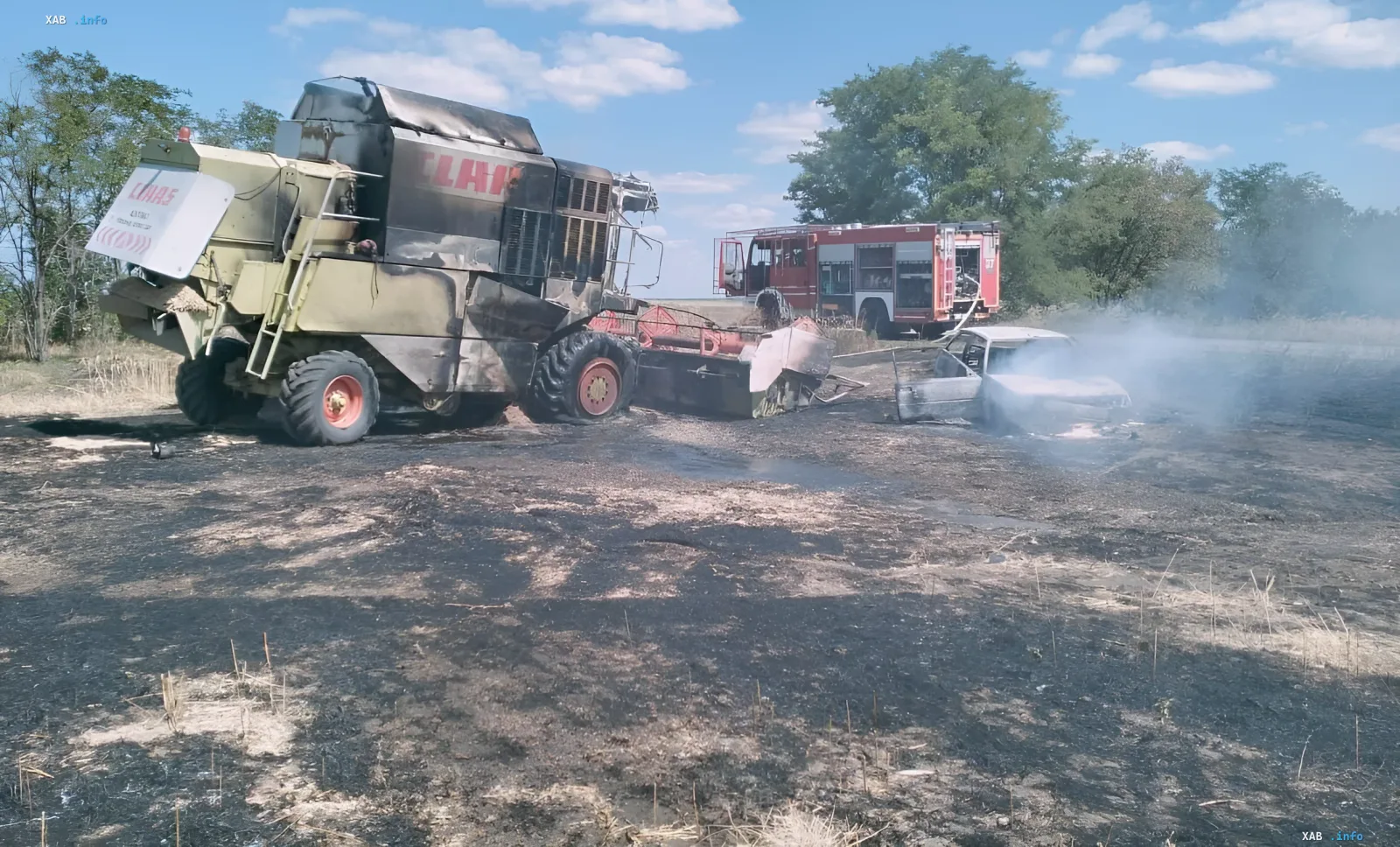 Folgen des Drohnenangriffs: zerstörte landwirtschaftliche Technik und Fahrzeug Verbrannter CLAAS-Mähdrescher und PKW nach Drohnenangriff in der Region Saporischschja, Feuerwehrfahrzeug löscht nahegelegene Restbrände