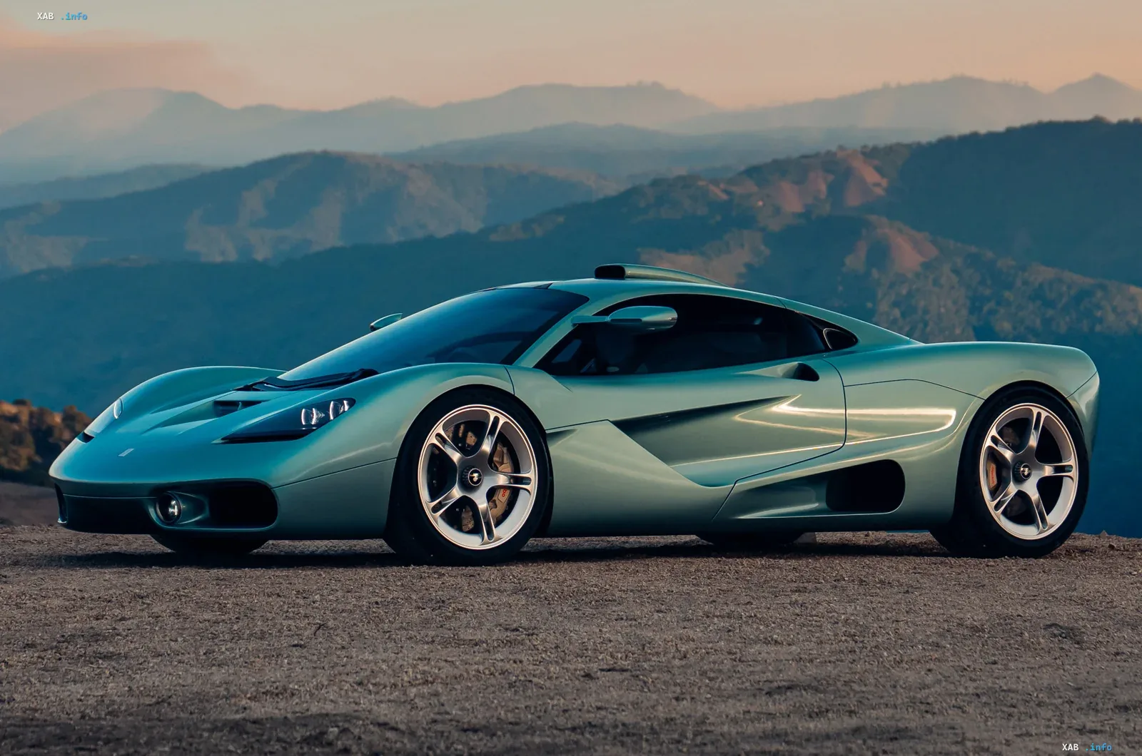 Новый суперкар Gordon Murray Automotive T.50s в светло-зеленом цвете на фоне гор, демонстрирующий наследие McLaren F1 и комфорт для дальних поездок