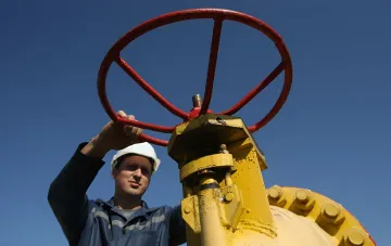 Рабочий в каске управляет красным вентилем на желтом газовом оборудовании на фоне синего неба