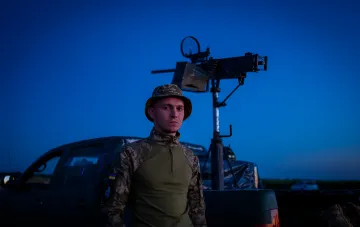 Украинский военный у зенитной установки на фоне ночного неба, готовый к отражению массовой атаки дронов