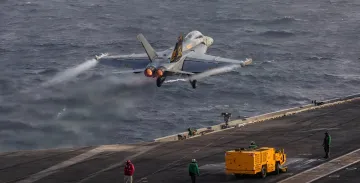 F/A-18 Hornet-Jagdflugzeug startet von der Flugdecke eines US-Marine-Flugzeugträgers vor stürmischem Meer, was die angespannte Situation mit Logistikproblemen und Personalmangel im Nahen Osten veranschaulicht