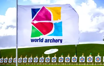 Флаг World Archery на фоне мишеней для стрельбы из лука, символизирующий отмену санкций против российских стрелков