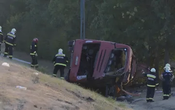 Zertrümmerter roter Bus nach dem Umkippen am Straßenrand in Ungarn, Rettungskräfte untersuchen den Ort des tragischen Unfalls